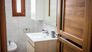 Un baño con lavamanos blanco, mueble de madera y un espejo encima.