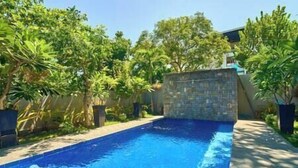 A swimming pool with a stone wall and lush greenery surrounding it. - Dos Maya by Araw Residences (Nasugbu)