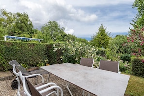 Un área de comedor al aire libre con una mesa y sillas, rodeada de vegetación exuberante y vista al cielo.