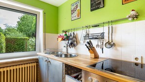 Een keuken met een raam, een gootsteen, een fornuis en een rek met keukengerei.