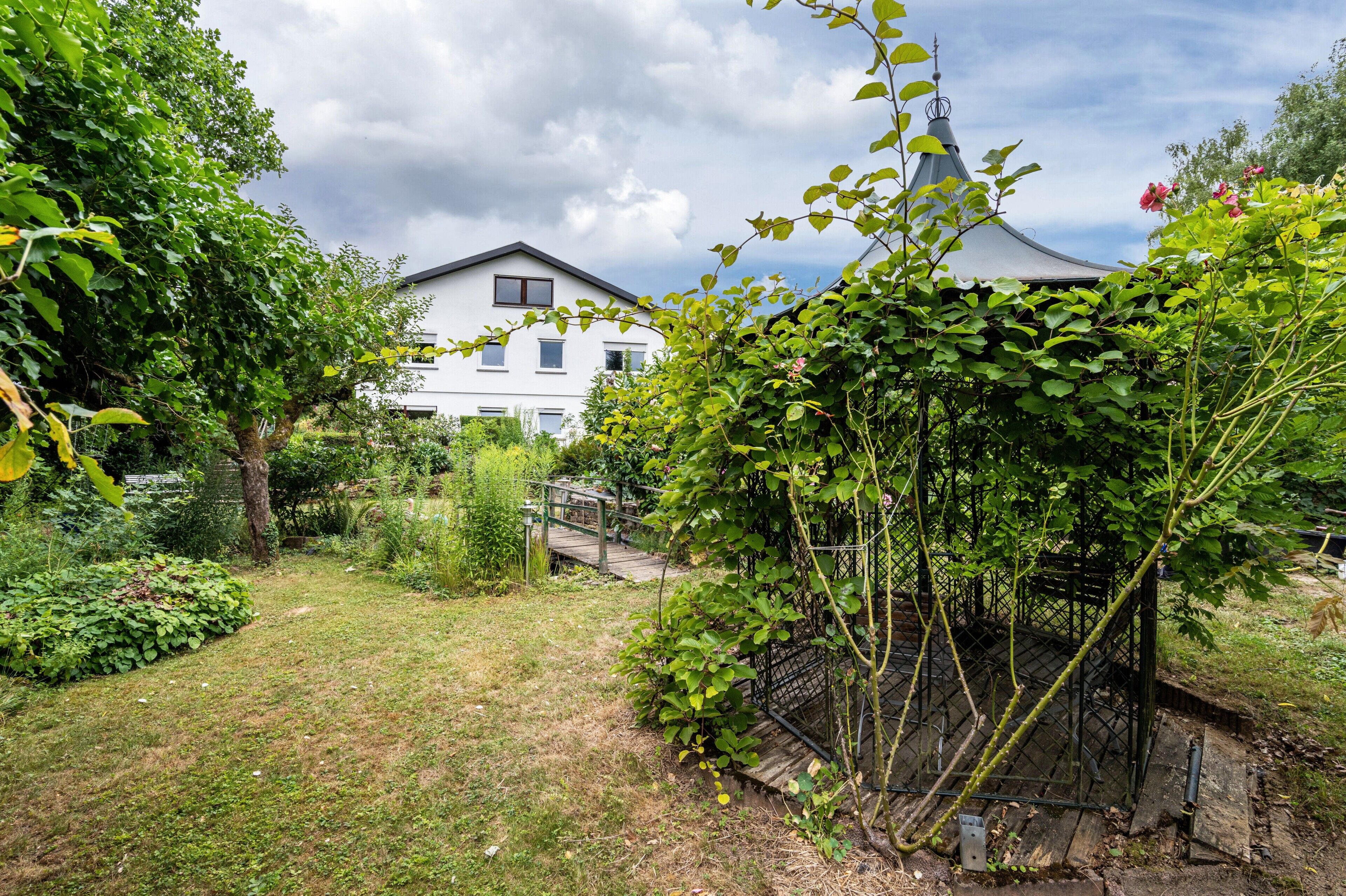 Ein Wohnhaus mit Garten, einer Holzbrücke und einem weißen Haus mit grauem Dach.