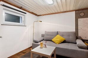 A room with a grey sofa, a small white table, a floor lamp, a window, and a wall-mounted radiator. - Sleep and Go Guesthouse with Shared Garden and Wi-Fi (Mundelsheim)