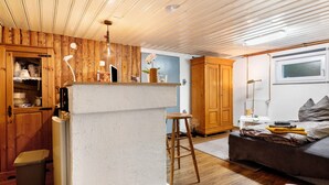 Ein Zimmer mit Holzboden, einem Bett mit grauer Decke, einem Holzschrank und einer weißen Wand mit Fenster.