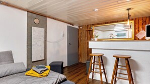 Ein modernes Zimmer mit einem Bett, Holzakzenten, einer kleinen Küchenzeile und einem Spiegel über der Arbeitsfläche.