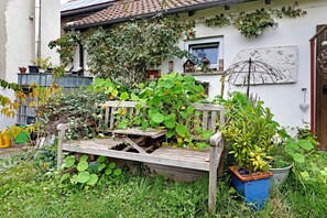 A garden with a wooden bench, potted plants, and a wall-mounted sculpture. - Sleep and Go Guesthouse with Shared Garden and Wi-Fi (Mundelsheim)