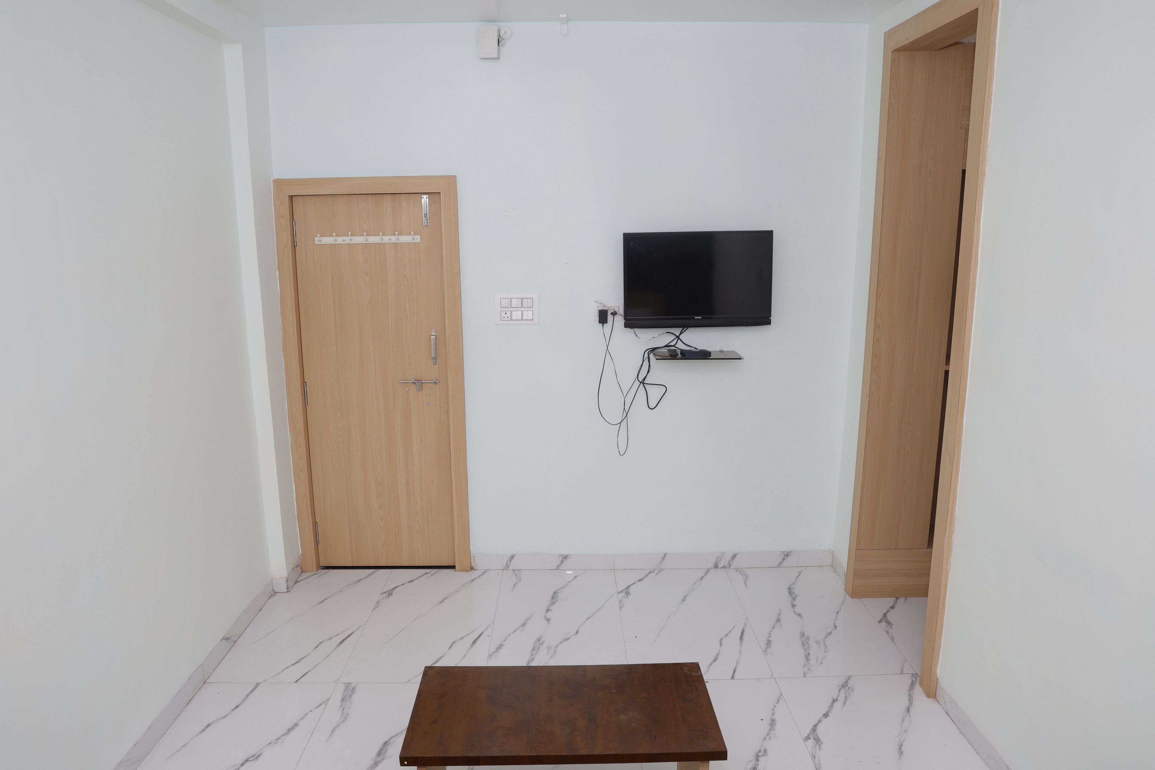 Een kamer met een houten deur, een aan de muur bevestigde televisie en een kleine tafel in het midden.