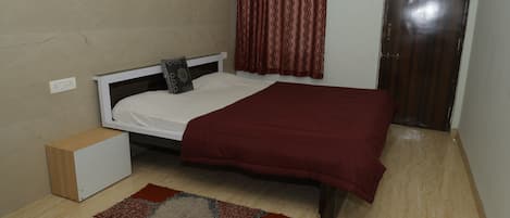 Un dormitorio con una cama, una mesita de noche, una cortina roja y una puerta.