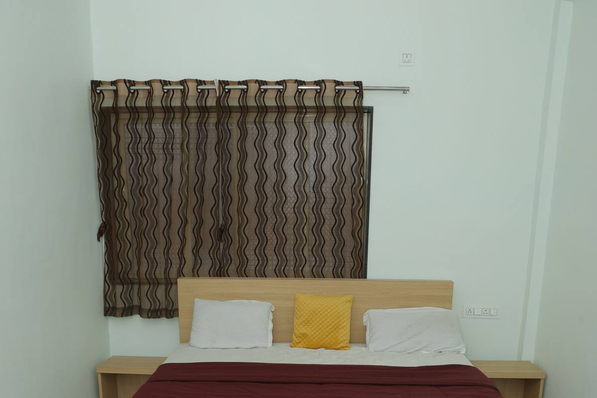 Ein Schlafzimmer mit Bett, Nachttischen, einem Holznachtkästchen, einem Marmorboden und einem Vorhang mit Wellenmuster.