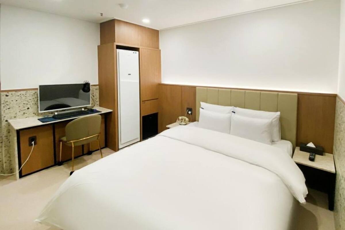 A hotel room with a bed, a desk with a computer, a telephone, and a minibar.