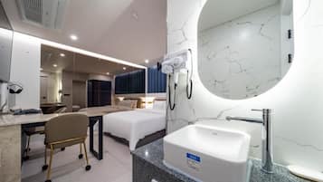 Habitación de hotel con cama, escritorio, silla y baño con lavamanos y espejo.