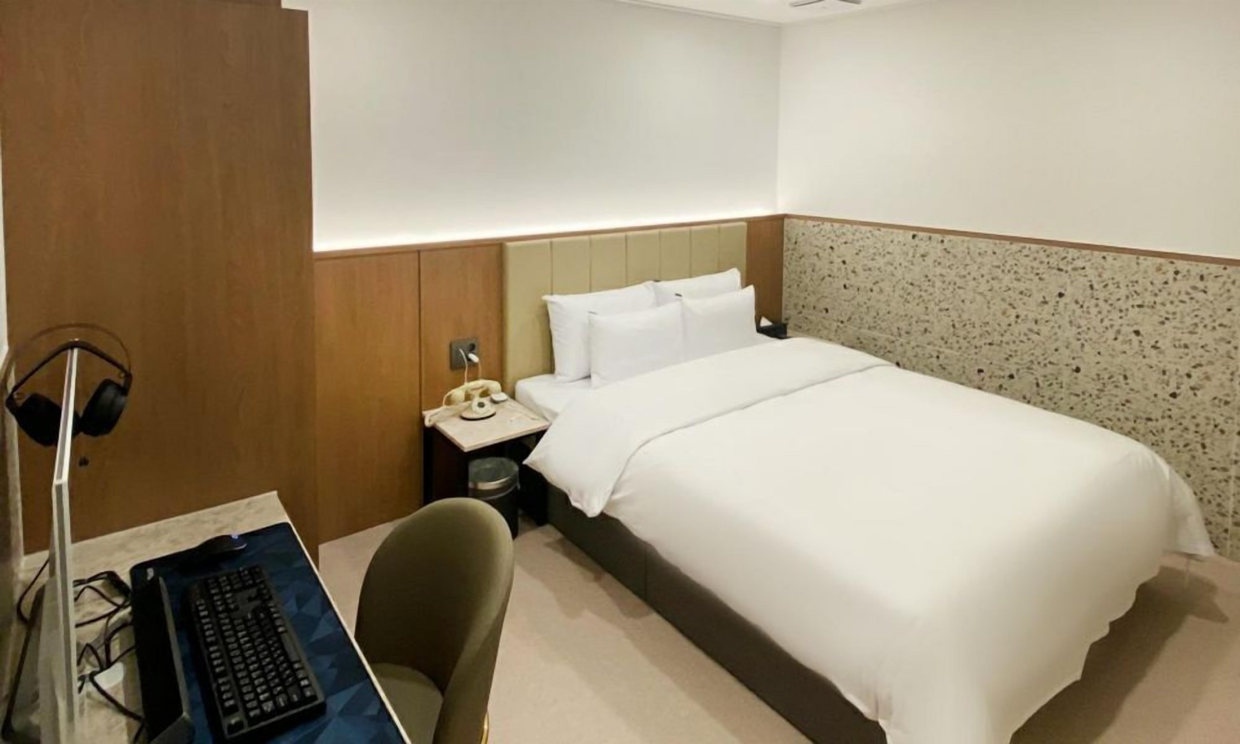 Habitación de hotel con cama, escritorio con computadora, silla, teléfono y auriculares.