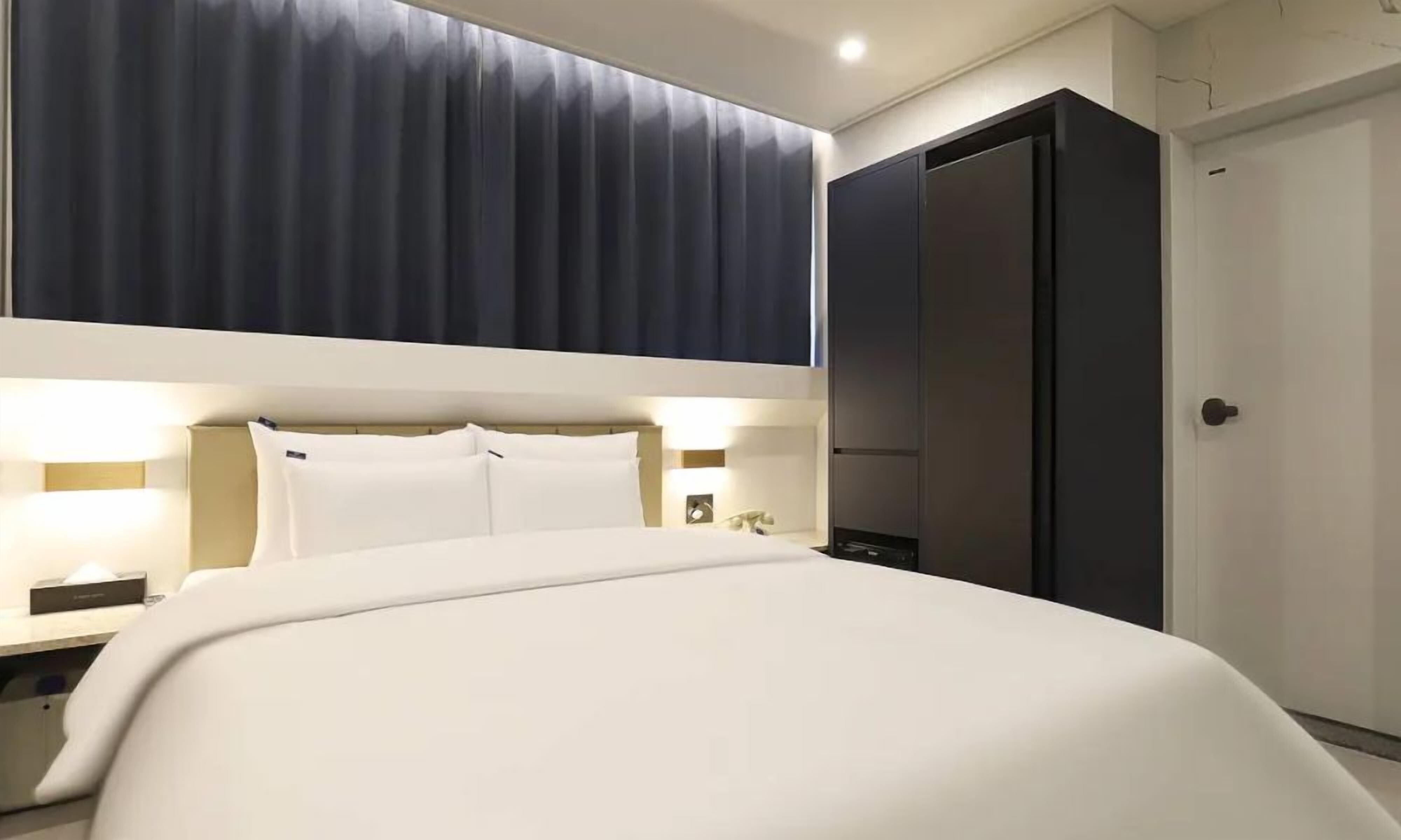 A hotel room with a large bed, bedside tables, a wardrobe, and a door.