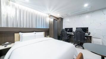 Quarto de hotel com uma cama grande, duas mesas com computadores e design moderno.