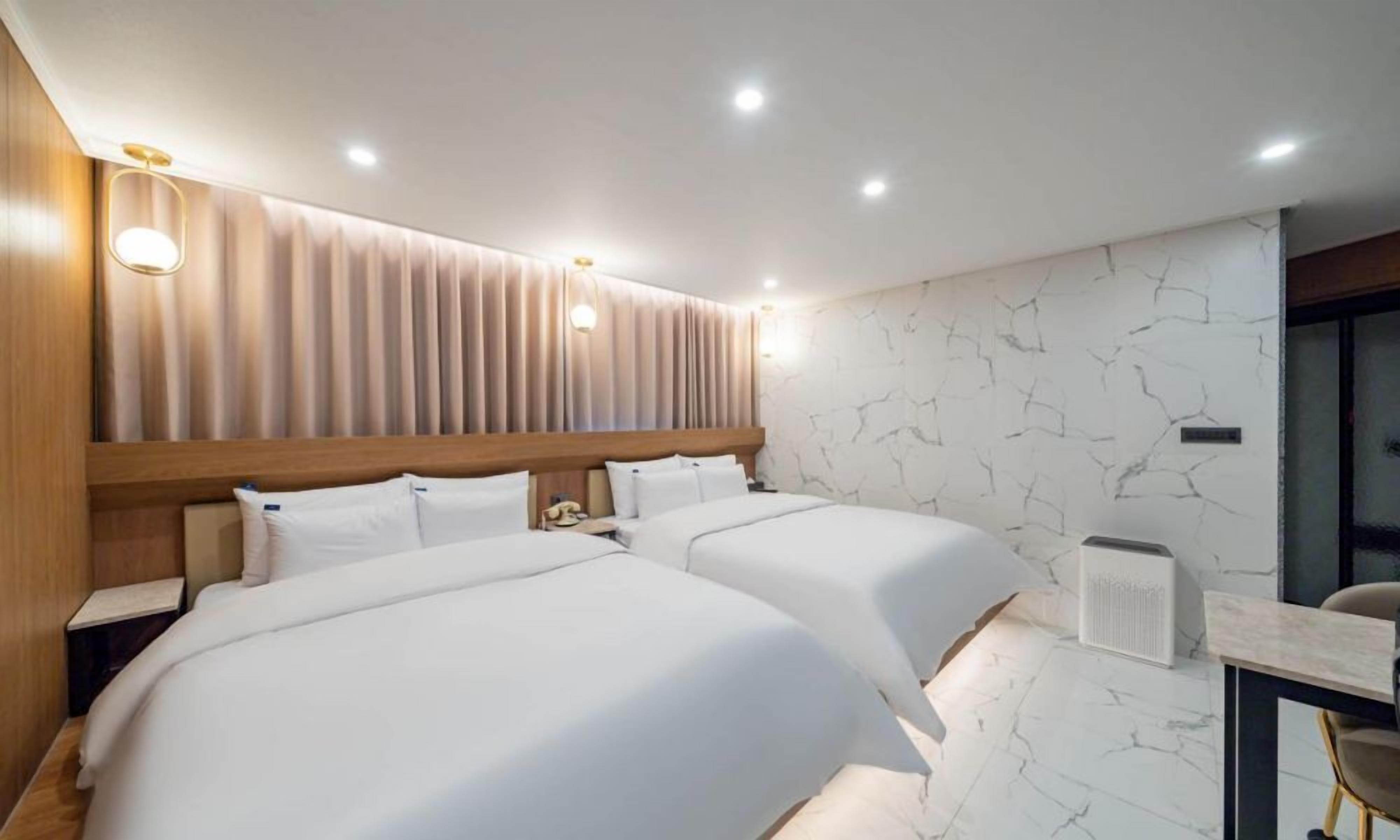 A modern hotel room with two beds, a wooden headboard, a marble-patterned wall, and a desk with a chair.