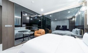 Una habitación de hotel moderna con una cama grande, una zona de estar con una silla, una mesita y un espejo amplio.