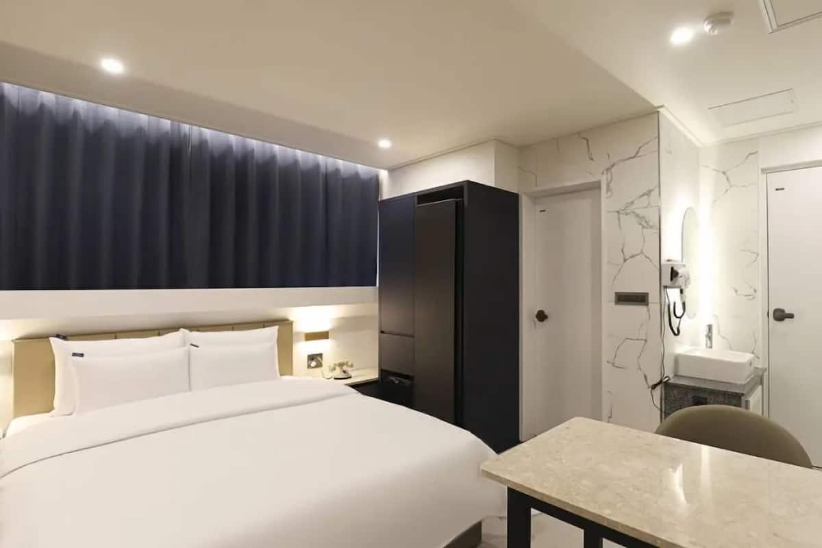 A hotel room with a large bed, a desk, a wardrobe, and a bathroom with a marble wall.
