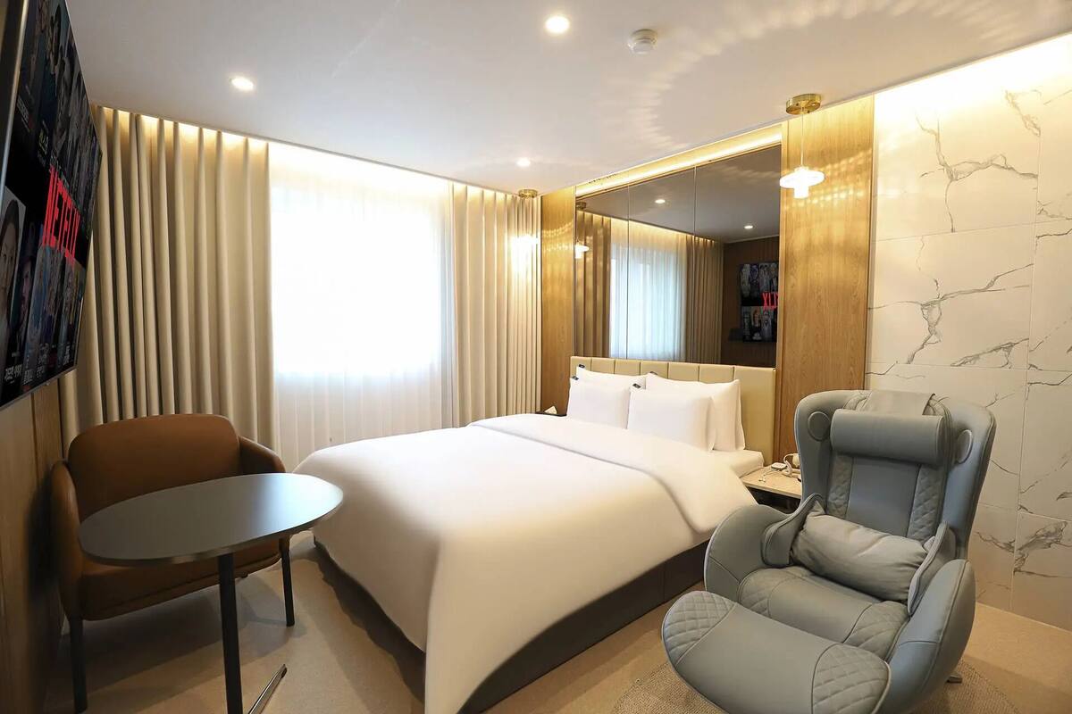 A hotel room with a bed, a desk, a chair, and a large mirror.