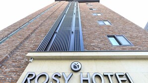 Exterior del Hotel Rosy, con fachada de ladrillo moderno y una destacada estructura metálica vertical.