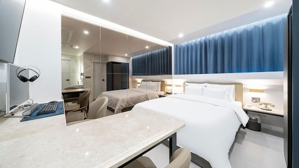 Una habitación de hotel moderna con una cama grande, un escritorio con computadora y una zona de estar separada.