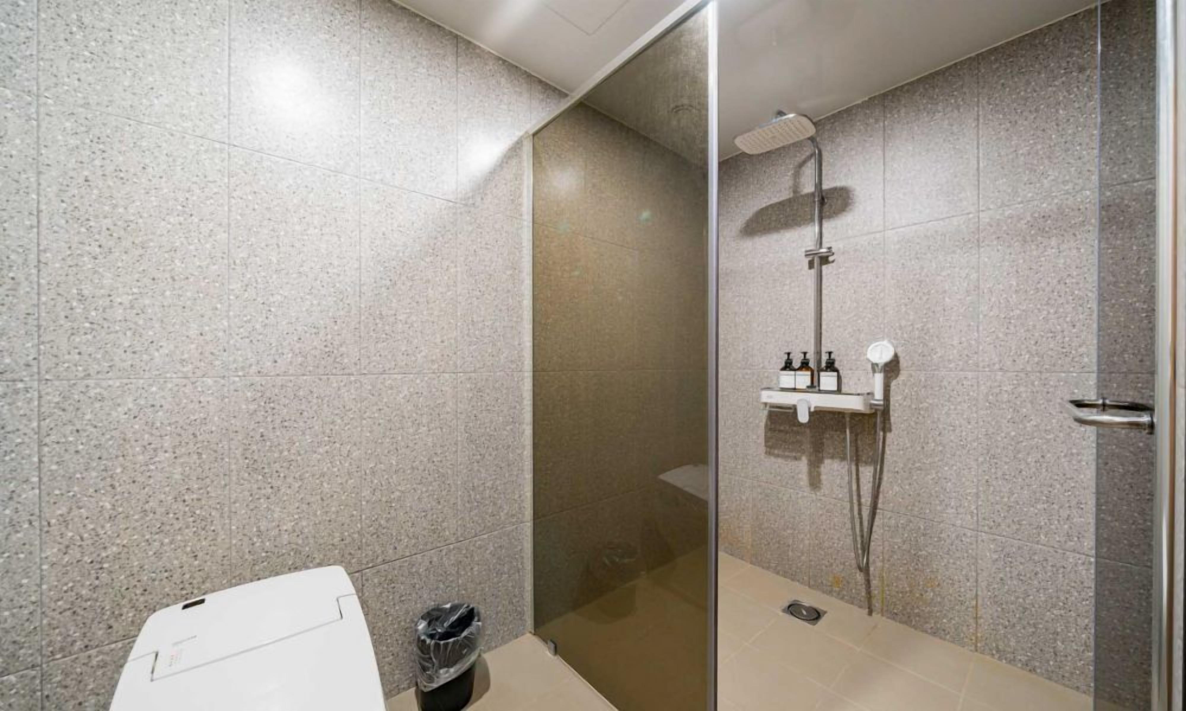 A modern bathroom with a shower, a toilet, and a trash bin.