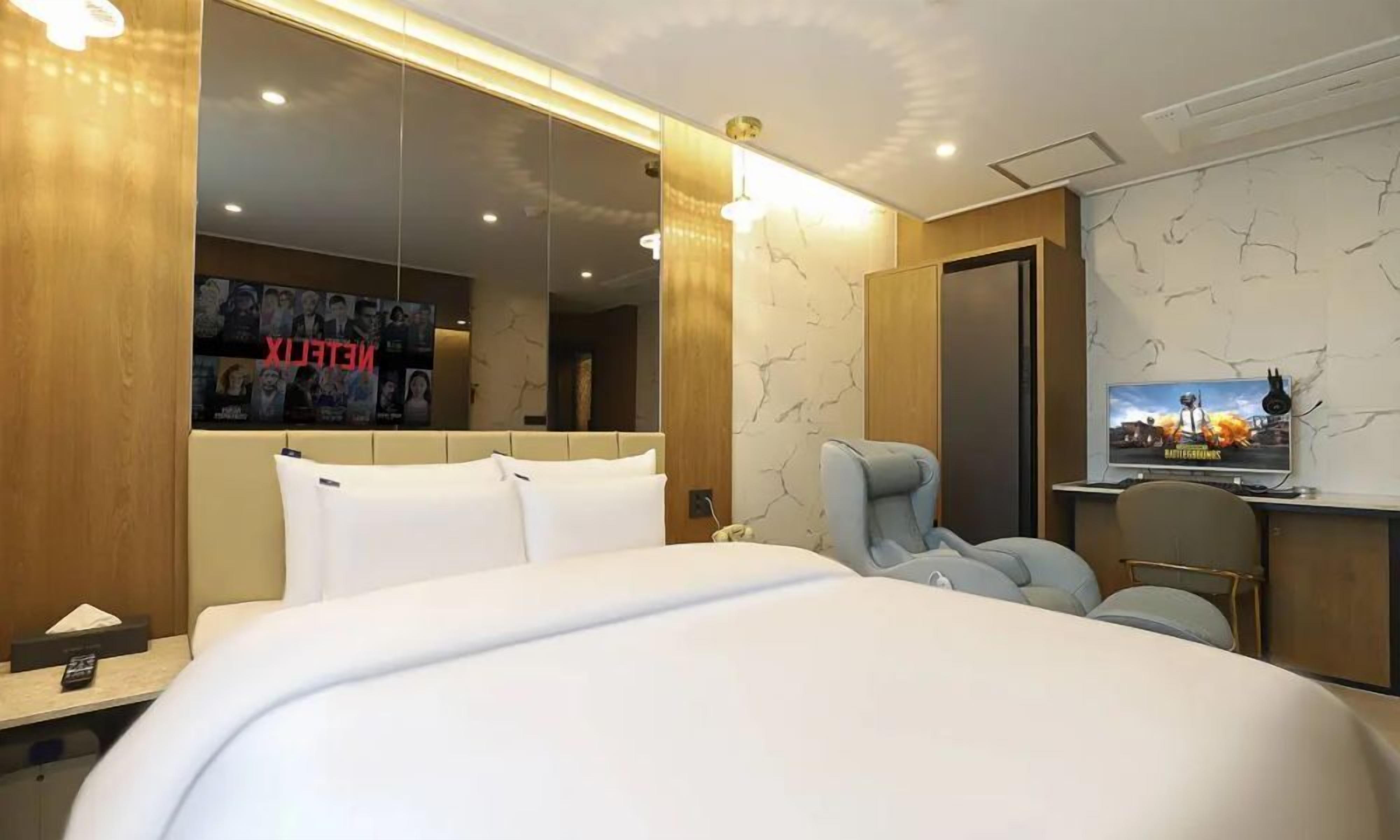 A modern hotel room with a large bed, a seating area, a TV, and a poster on the wall.
