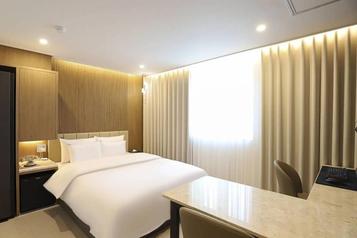A hotel room with a bed, bedside table, and a desk with a chair.