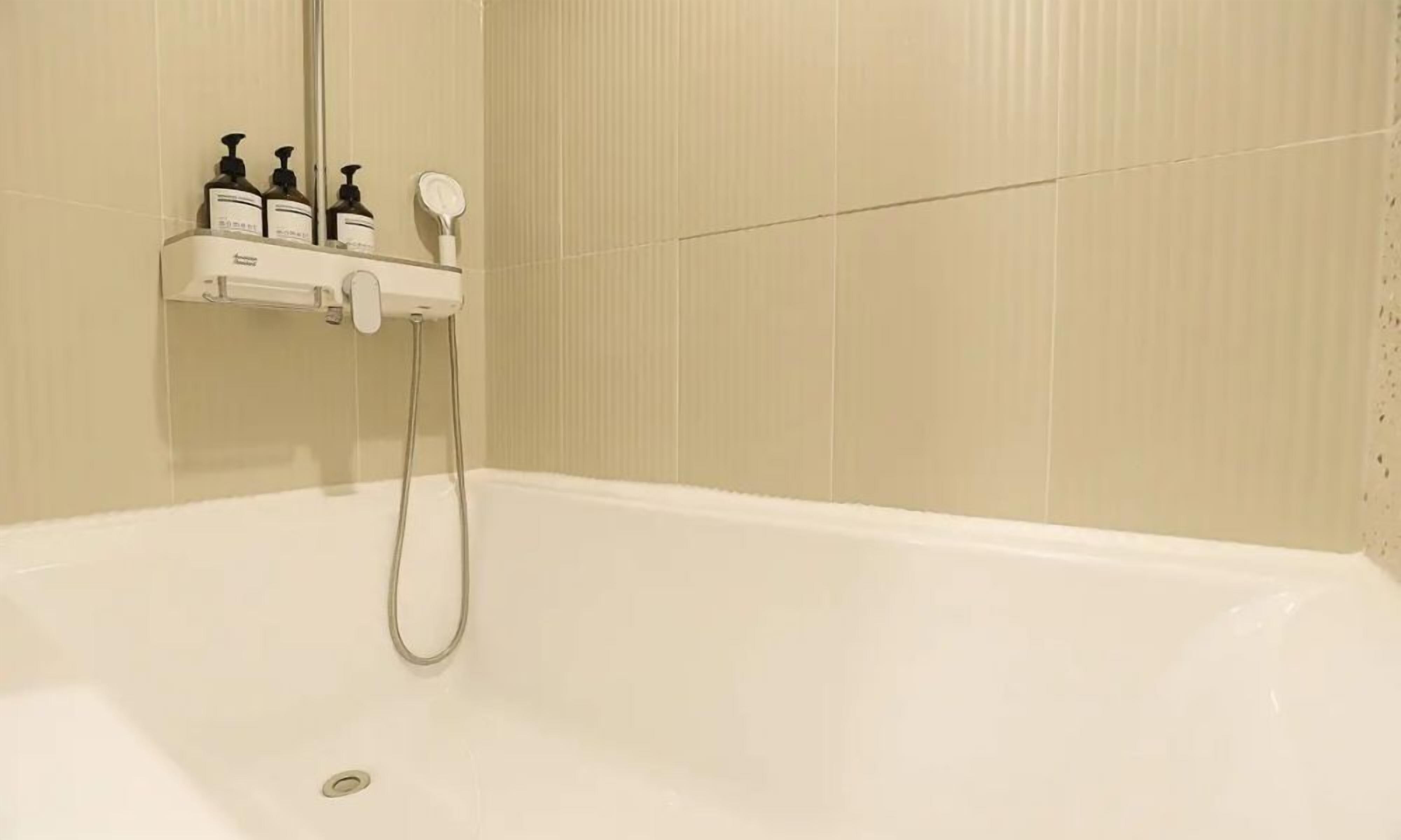 Una bañera blanca con un cabezal de ducha manual y una botella de champú en un estante.