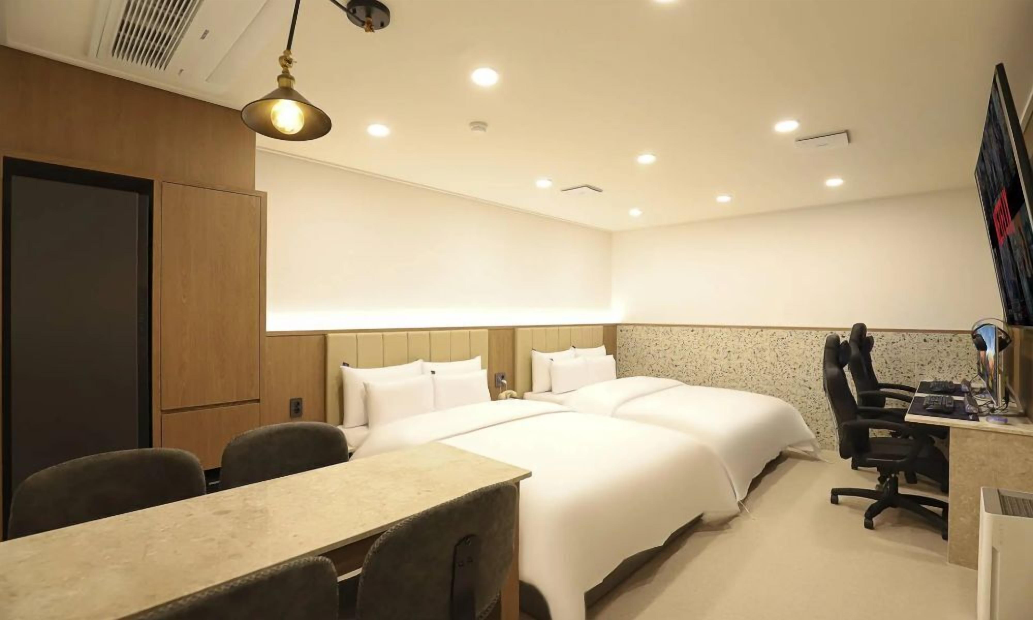 A hotel room with a bed, desk, chairs, and a computer.