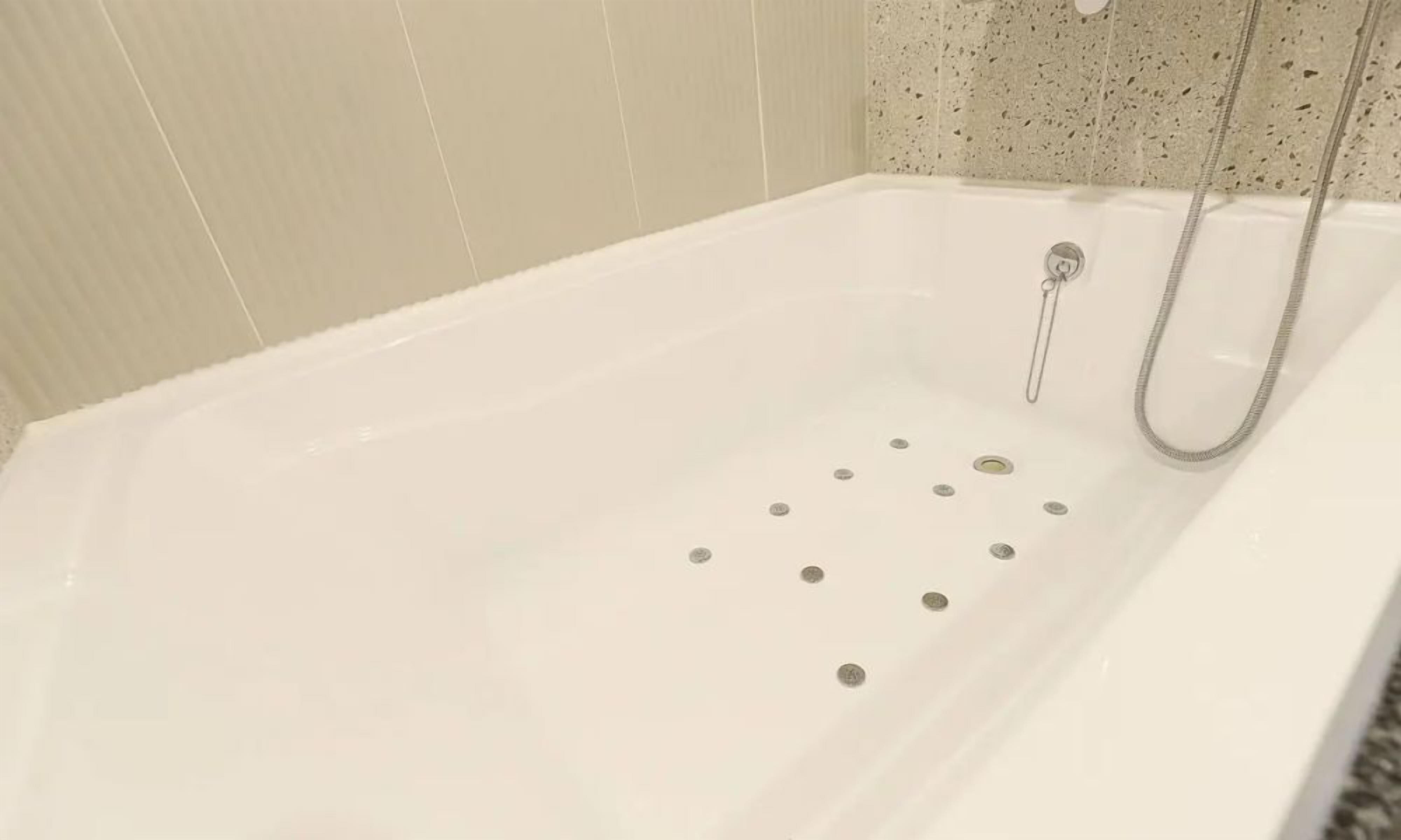 Une baignoire blanche dotée d’un pommeau de douche et de plusieurs trous d’évacuation.