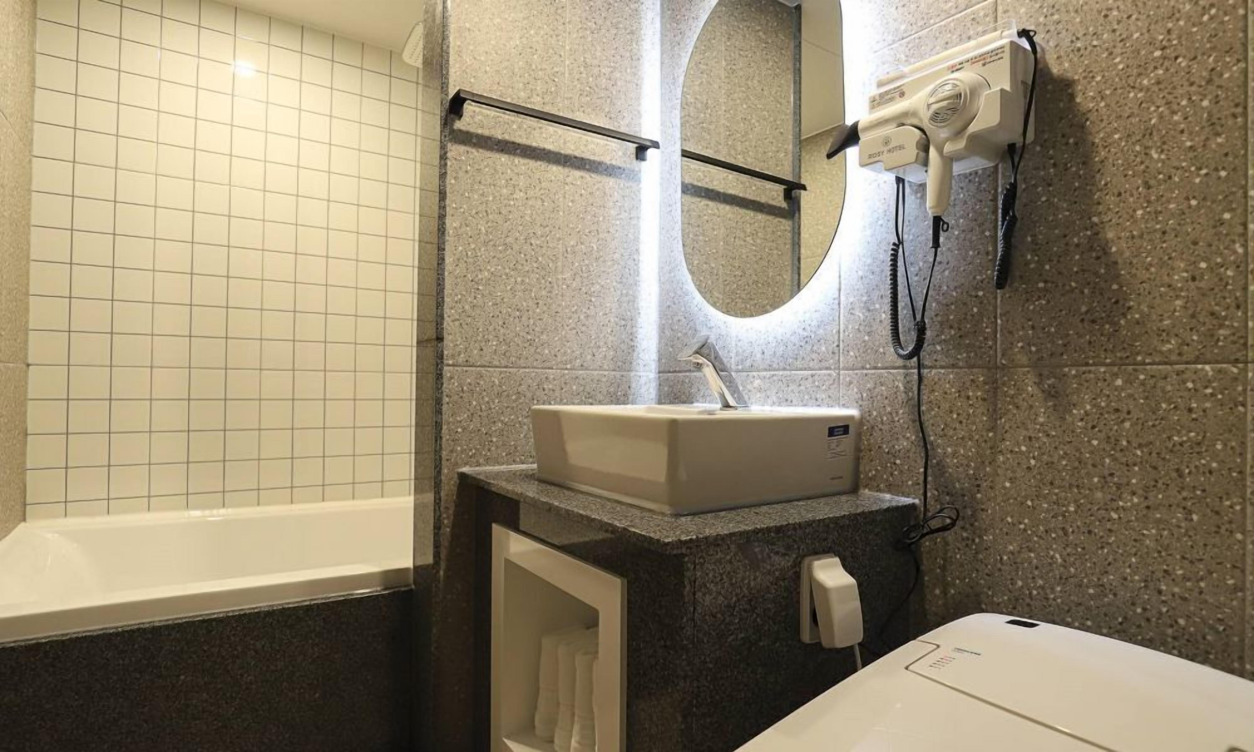 Ein Badezimmer mit Badewanne, Waschbecken, Spiegel und Fön an der Wand.