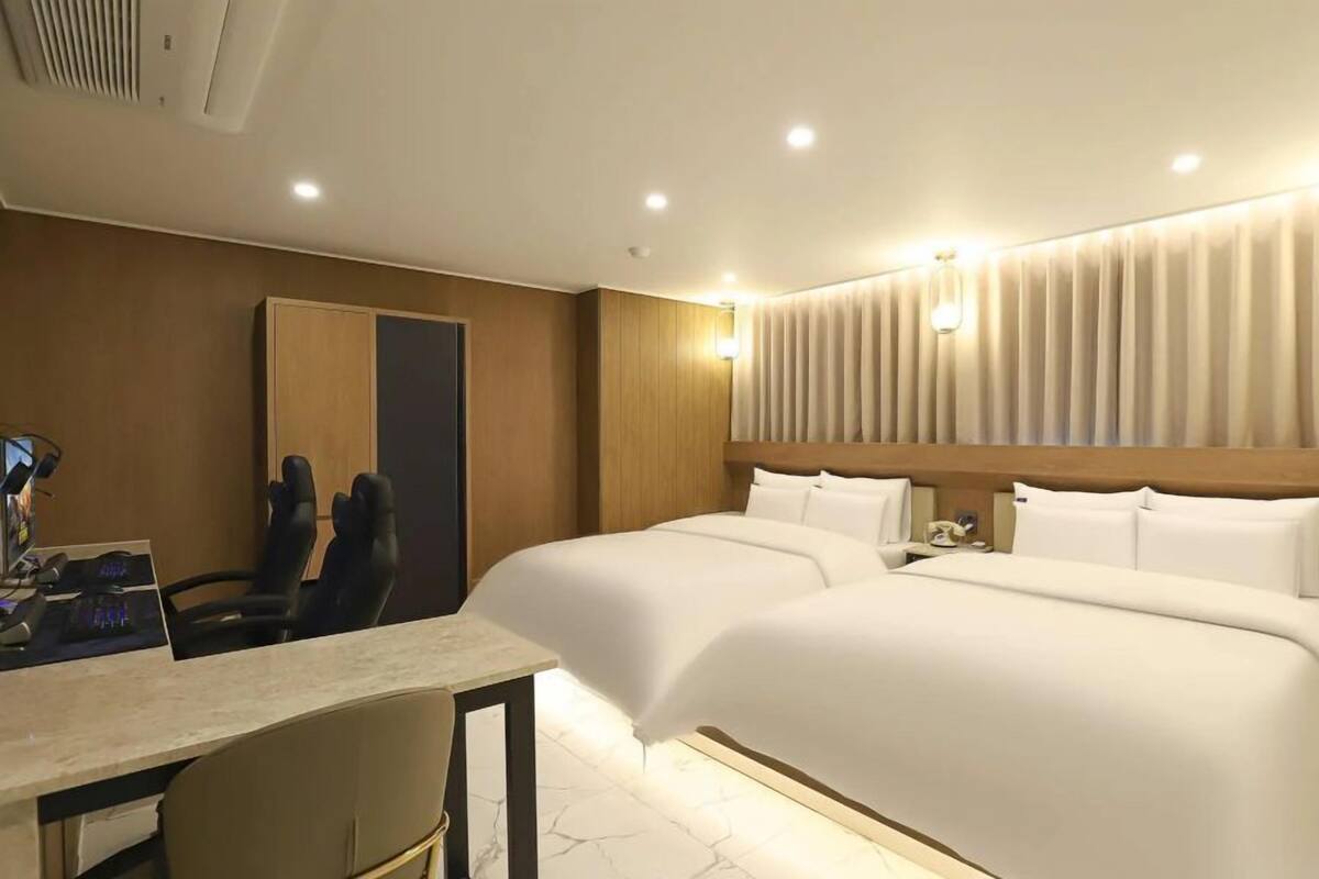 A hotel room with two beds, a desk, a chair, and a mirror.