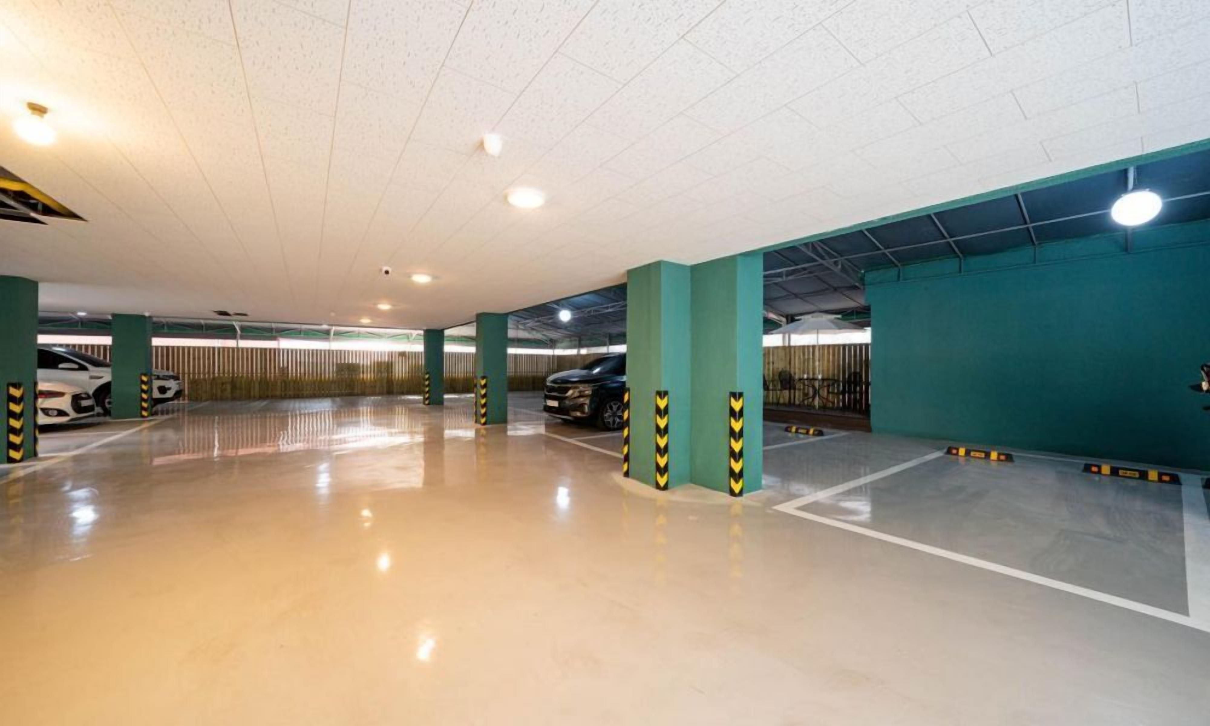 Un estacionamiento con varios niveles, suelo limpio y reflectante, y pilares verdes con marcas amarillas en forma de chevrón.