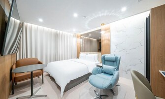Una habitación de hotel moderna con una cama, un sillón azul, una mesita y un espejo.