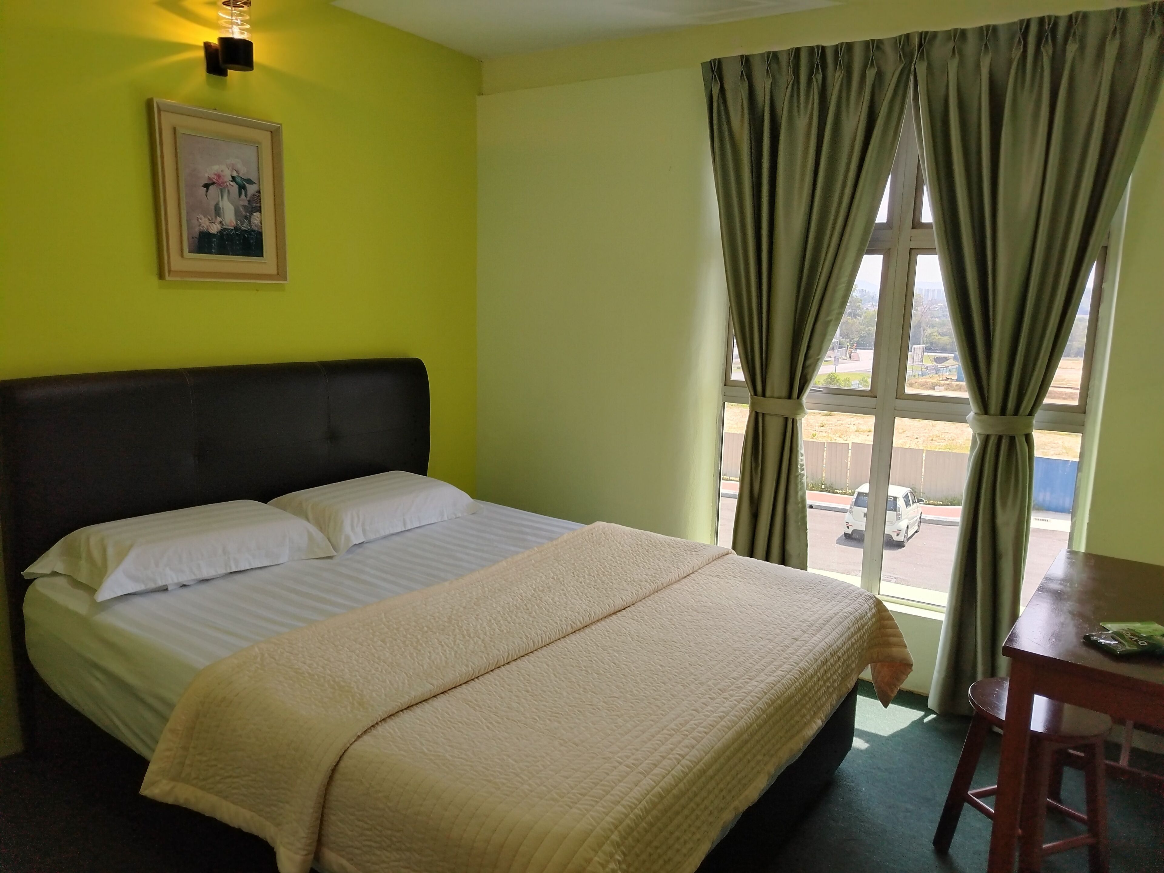 A hotel room with a bed, a painting on the wall, and a window with curtains.