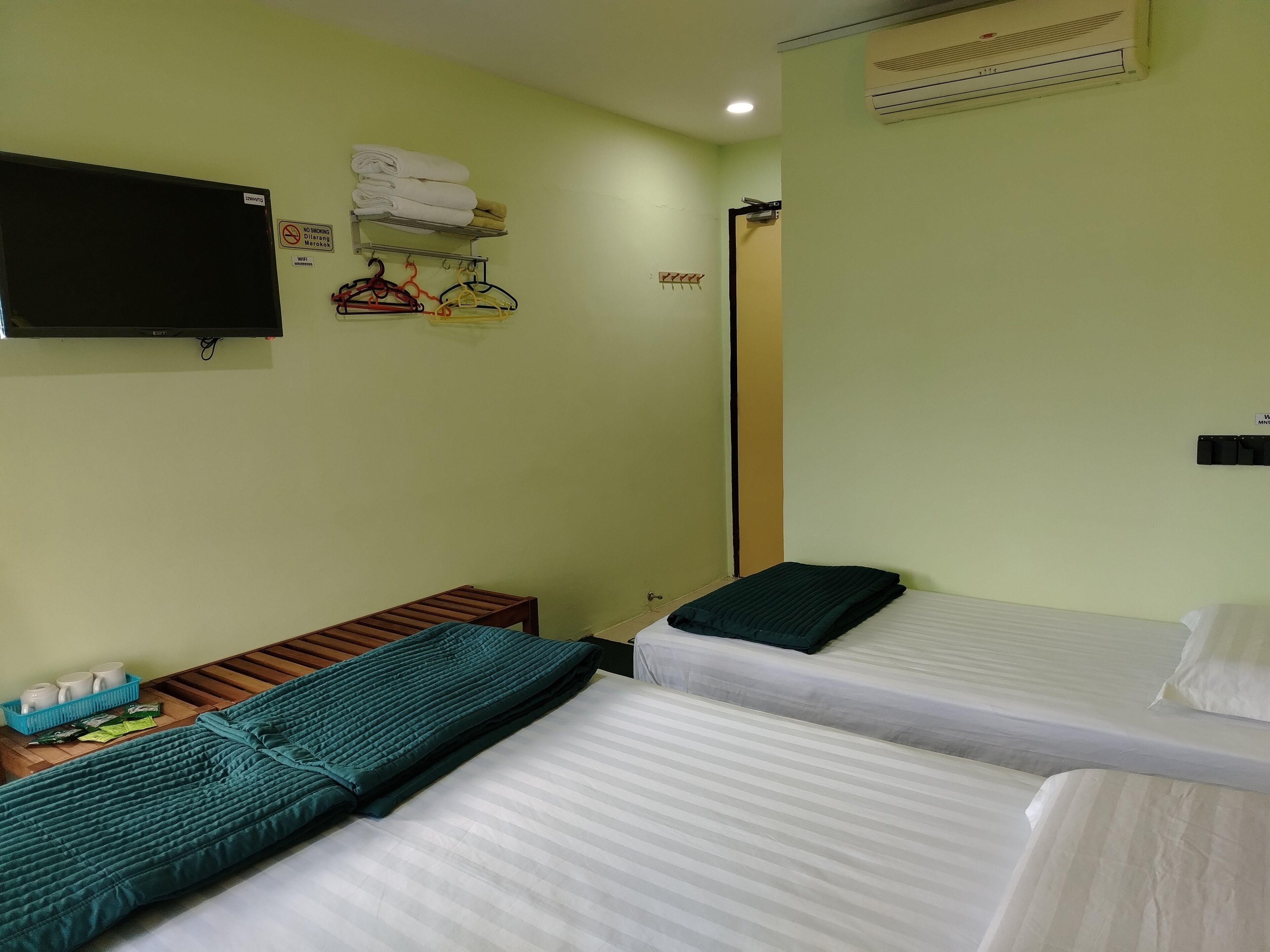 A hotel room with two beds, a TV, a shelf with folded towels, and a wall-mounted heater.