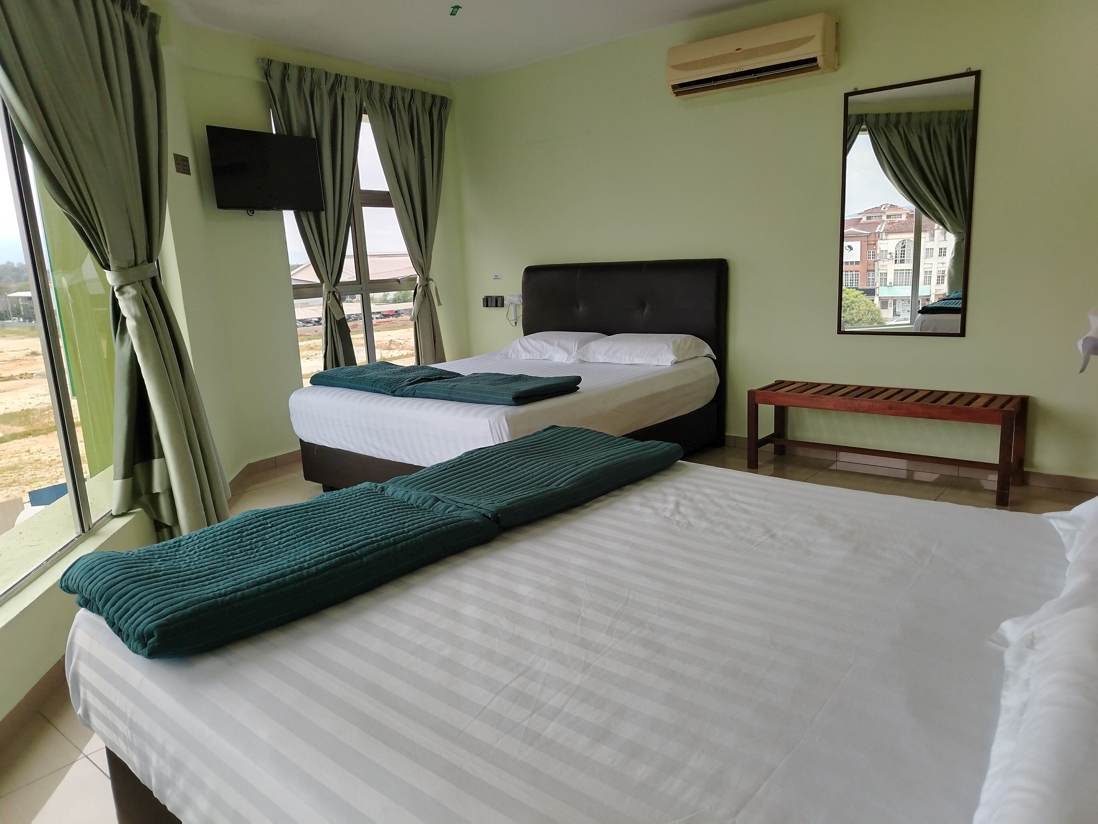 A hotel room with two beds, a bench, a TV, and a window with curtains.