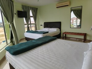 Camera d'albergo con due letti, una panca, una televisione e una finestra con tende.