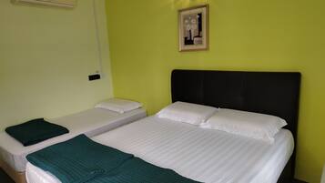 Quarto de hotel com duas camas de solteiro, uma cama grande, um cobertor verde, um quadro na parede e um ventilador de teto.