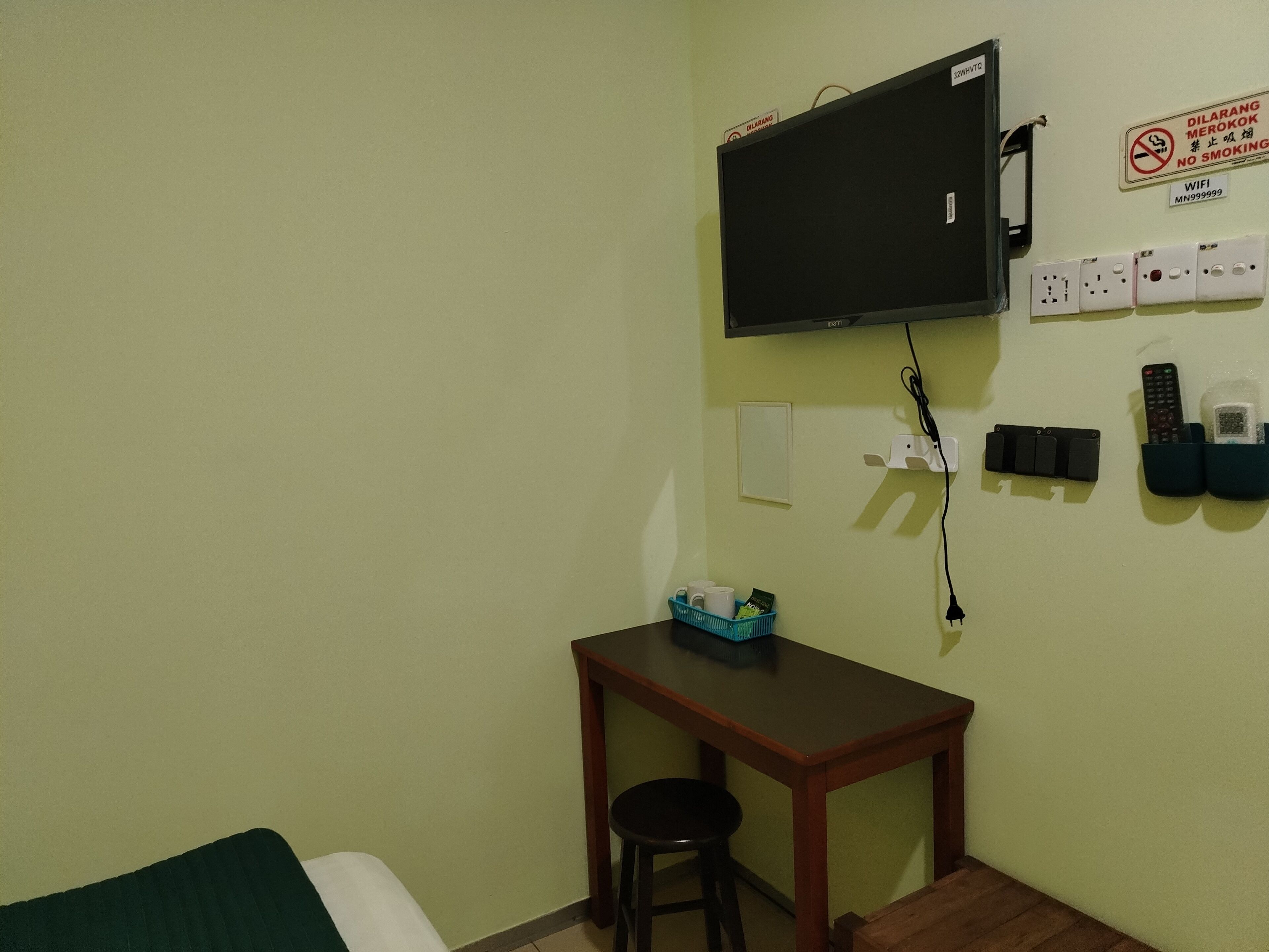 Una habitació petita amb televisió penjada a la paret, escriptori amb cadira i llit.