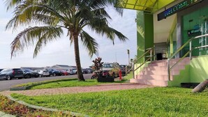 A parking area with cars, a palm tree, and a building with a green facade and a 'Welcome' sign. - Hotel O Seremban Near SnowLim Wonderland Formerly M&N Hotel (Seremban)
