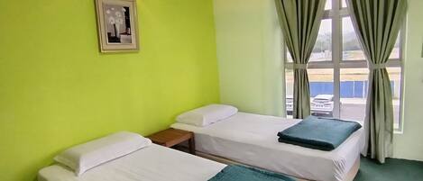 A hotel room with two single beds, a small bedside table, a framed picture on the wall, and a window with curtains.