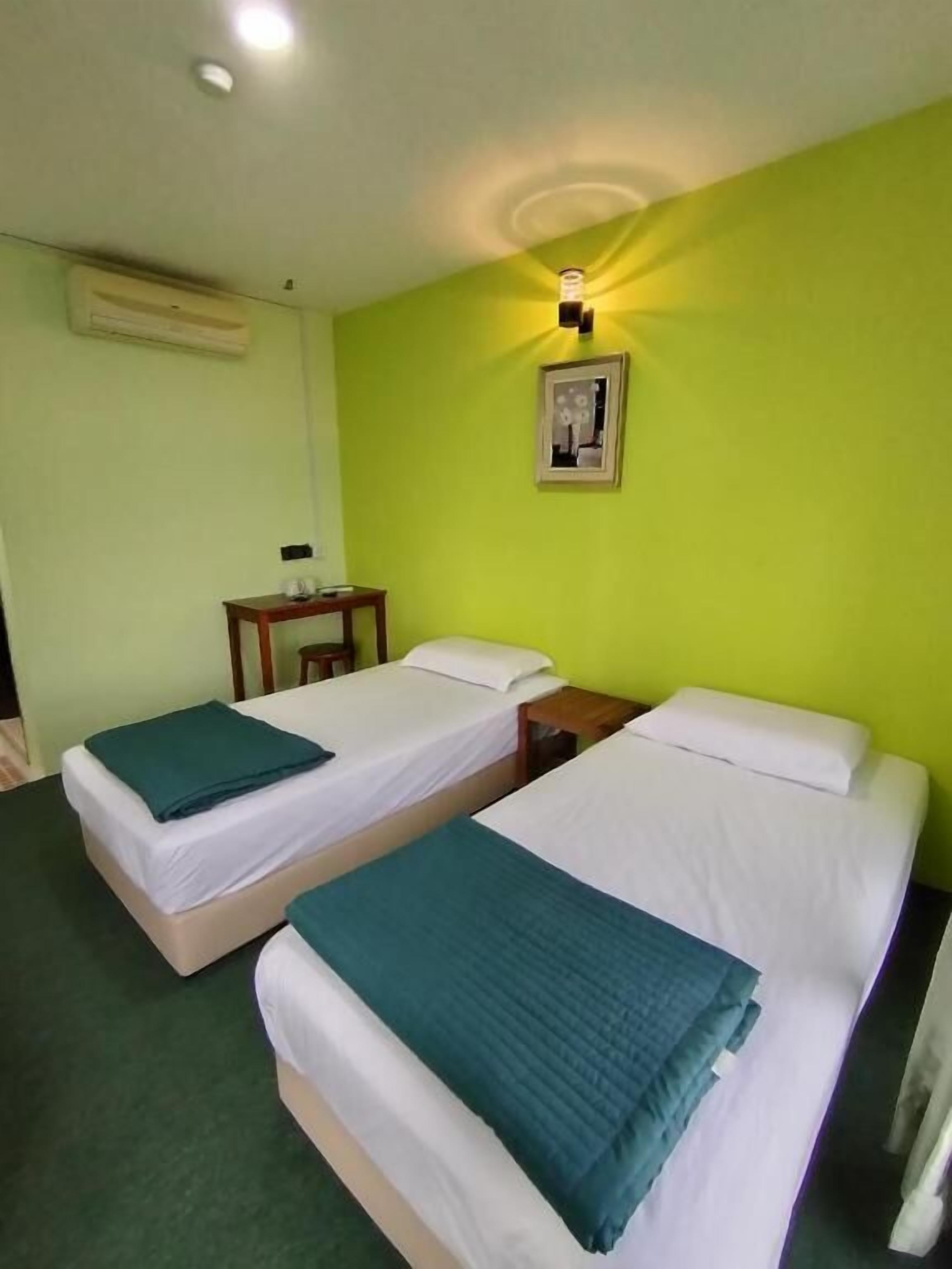A hotel room with two single beds, a small table, a chair, and a wall-mounted picture.