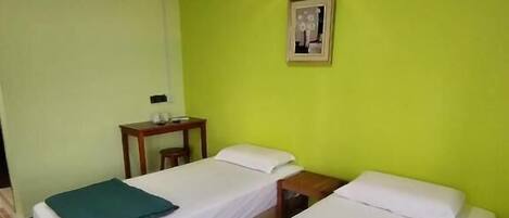 A hotel room with two single beds, a small table, a chair, and a wall-mounted picture.