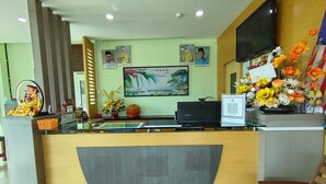 A hotel reception area with a modern design, featuring a reception desk, a flat-screen TV, framed pictures on the wall, and a floral arrangement. - Hotel O Seremban Near SnowLim Wonderland Formerly M&N Hotel (Seremban)