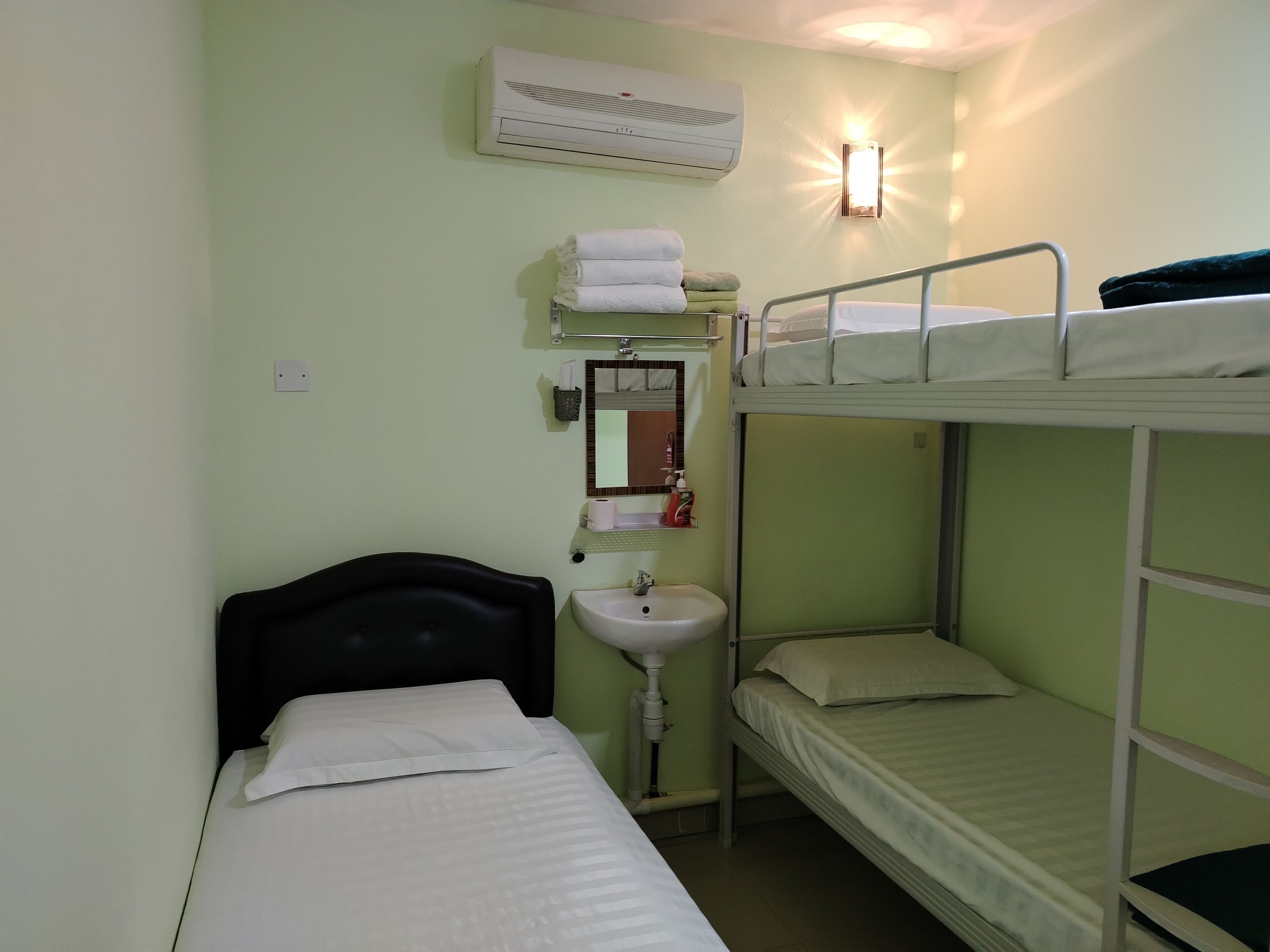Un alojamiento pequeño y con una sola habitación, con literas, una mesita de noche, aire acondicionado en la pared, un lavamanos y un espejo.