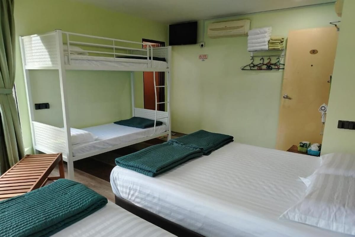 Una habitación con literas, una cama individual y un banco de madera.