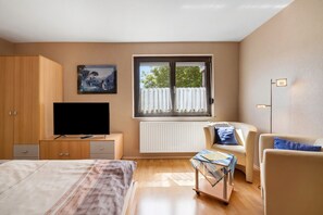 Een slaapkamer met een bed, een televisie, een bureau, een stoel, een raam met gordijnen en een radiator.