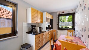 Et kompakt køkken med træskabe, en mikroovn, kaffemaskine og et spiseområde med bord og stole.
