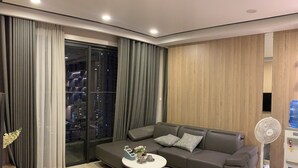 Ein modernes Wohnzimmer mit einem grauen Sofa, einem kleinen runden Tisch und einem großen Fenster mit Vorhängen.
