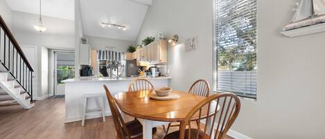 A modern kitchen with white cabinetry, a wooden dining table, and a staircase leading to another level.